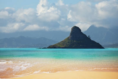 Mokoliʻi island, also known as Chinaman's Hat, rises high out of clear blue waters half a mile offshore of Oahu.